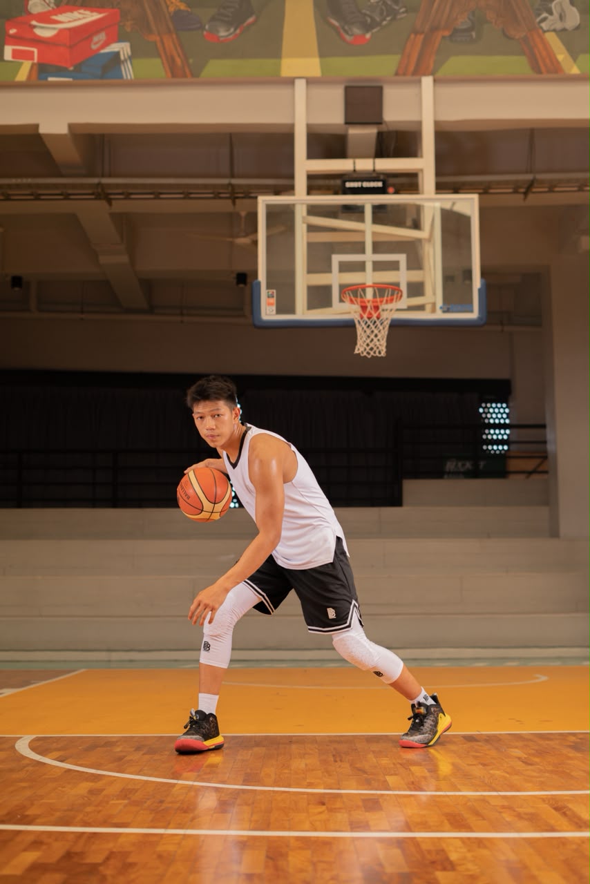 Frillian in a white jersey, dribbling a basketball on an indoor court
